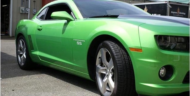  A green Camaro parked in front of a modern building, showcasing its sleek design and vibrant color.