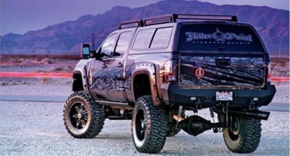 A truck with a prominent tire drives across the arid desert terrain.