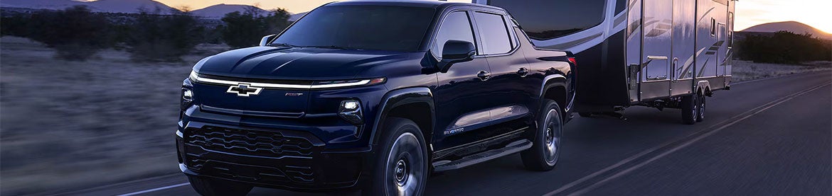 A 2021 Chevrolet Silverado driving down a scenic road surrounded by trees and open fields.