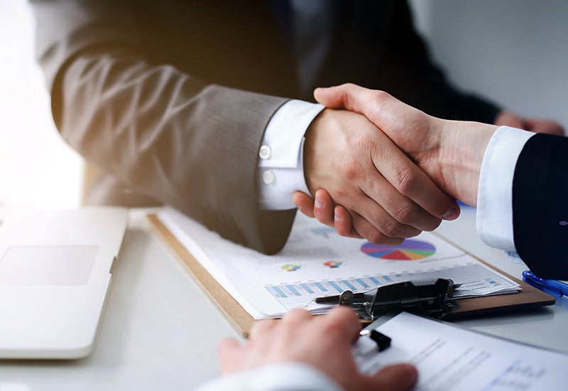 Two business professionals shaking hands over a desk
