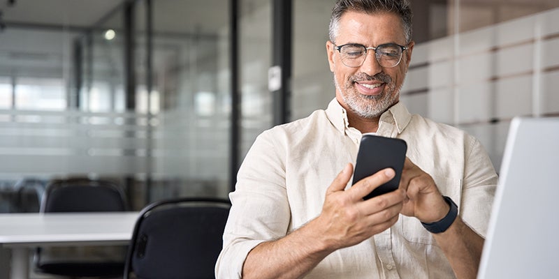 A man wearing glasses and a white shirt is focused on using his smartphone