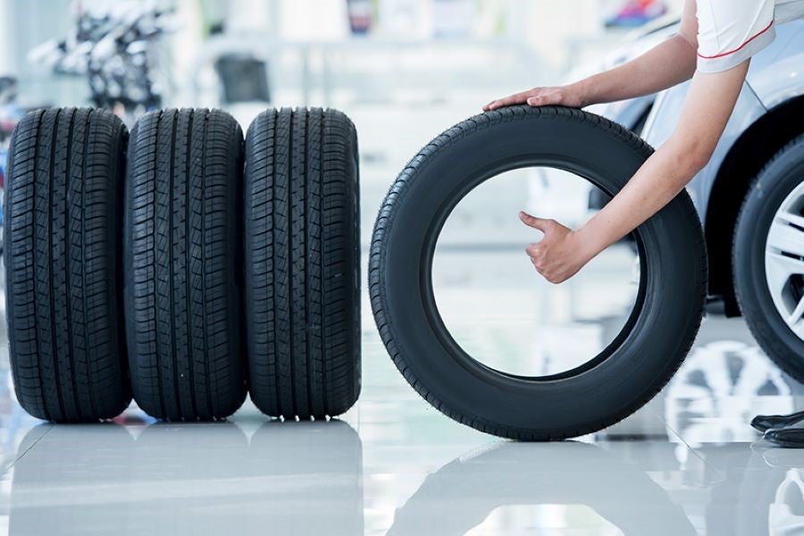 A man stands in front of a car, holding a tire with both hands, ready for maintenance or replacement.