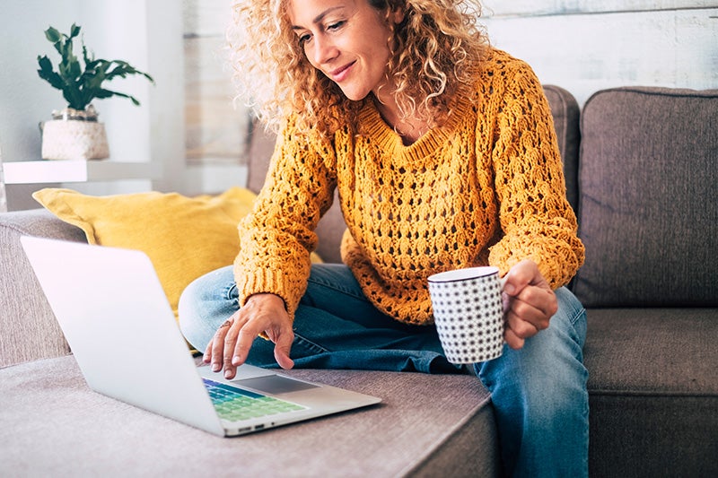 A woman holding a cup and using her laptop