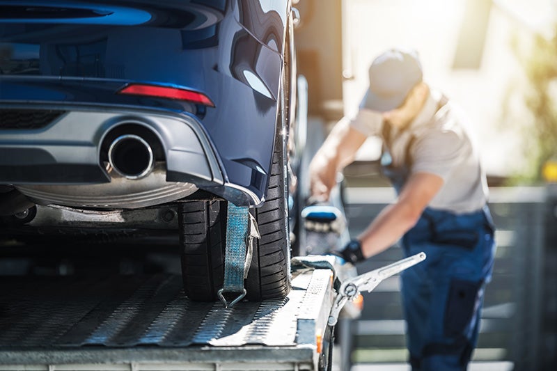 A man carefully loads a car onto a flatbed truck, ensuring secure placement for transport.